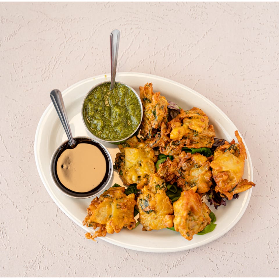 Plate of assorted crispy fritters served with green chutney and creamy dipping sauce.
