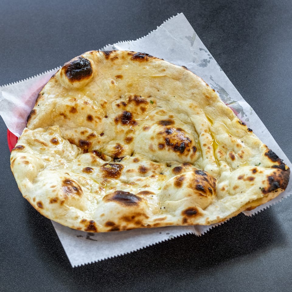 Golden-brown, blistered flatbread drizzled with oil rests on parchment paper atop a dark tabletop.