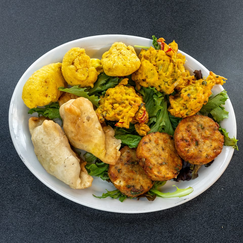 Plate of assorted golden fried appetizers, including samosas, fritters, and patties, served over leafy greens.