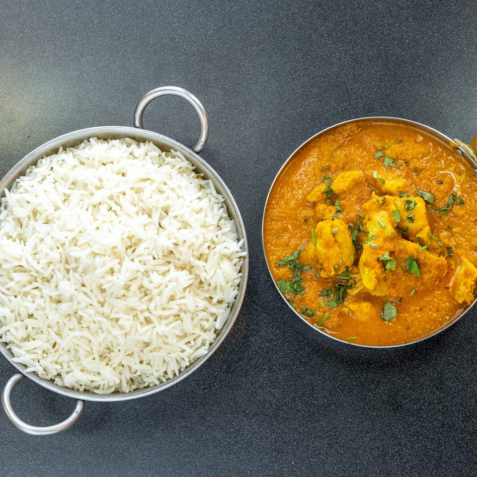 Overhead view of basmati rice and golden curry with chunks, garnished with cilantro, served in metal pans.
