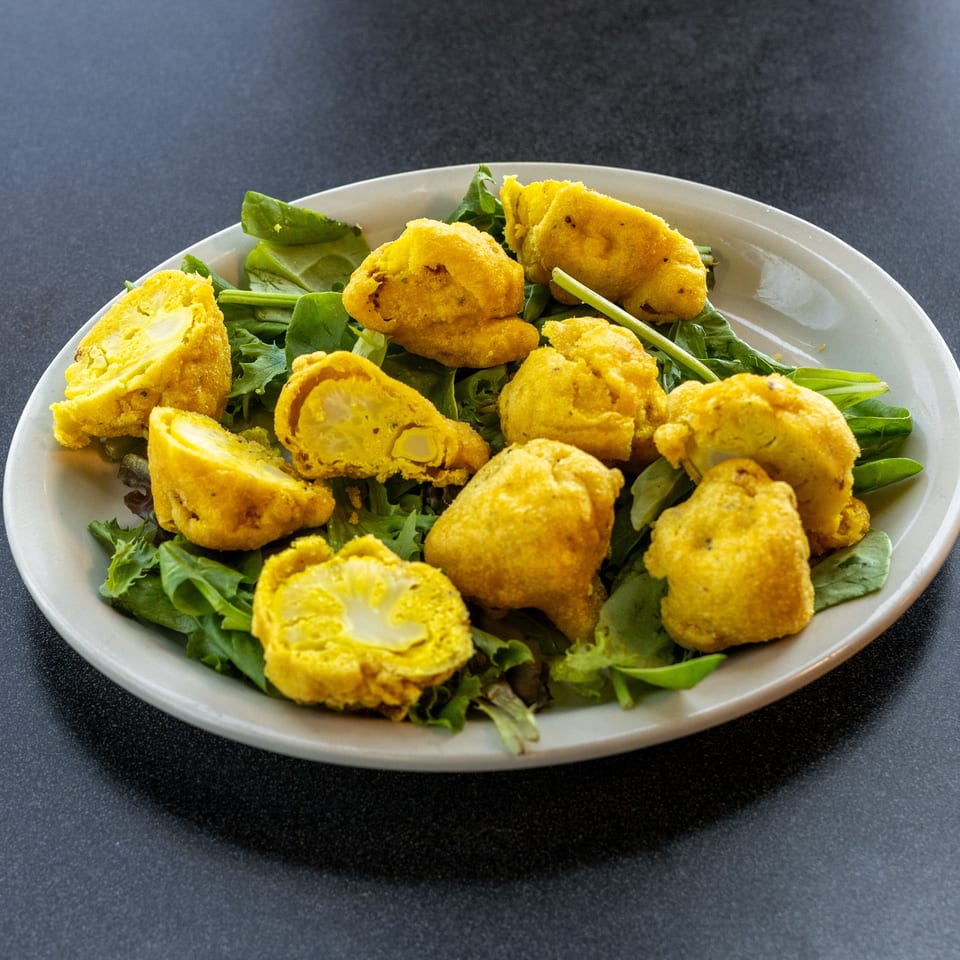 Golden battered vegetable fritters, some sliced open, arranged over fresh mixed greens on a white plate.