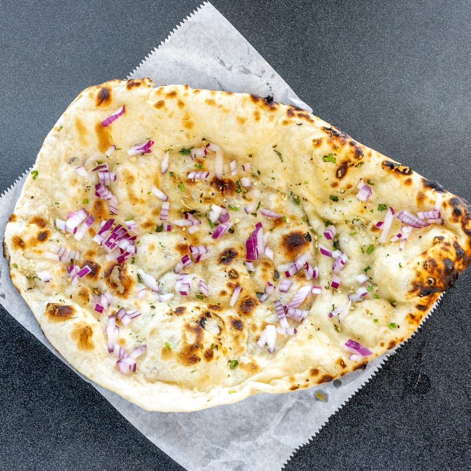 Grilled naan bread topped with chopped red onions and herbs, served on parchment paper.