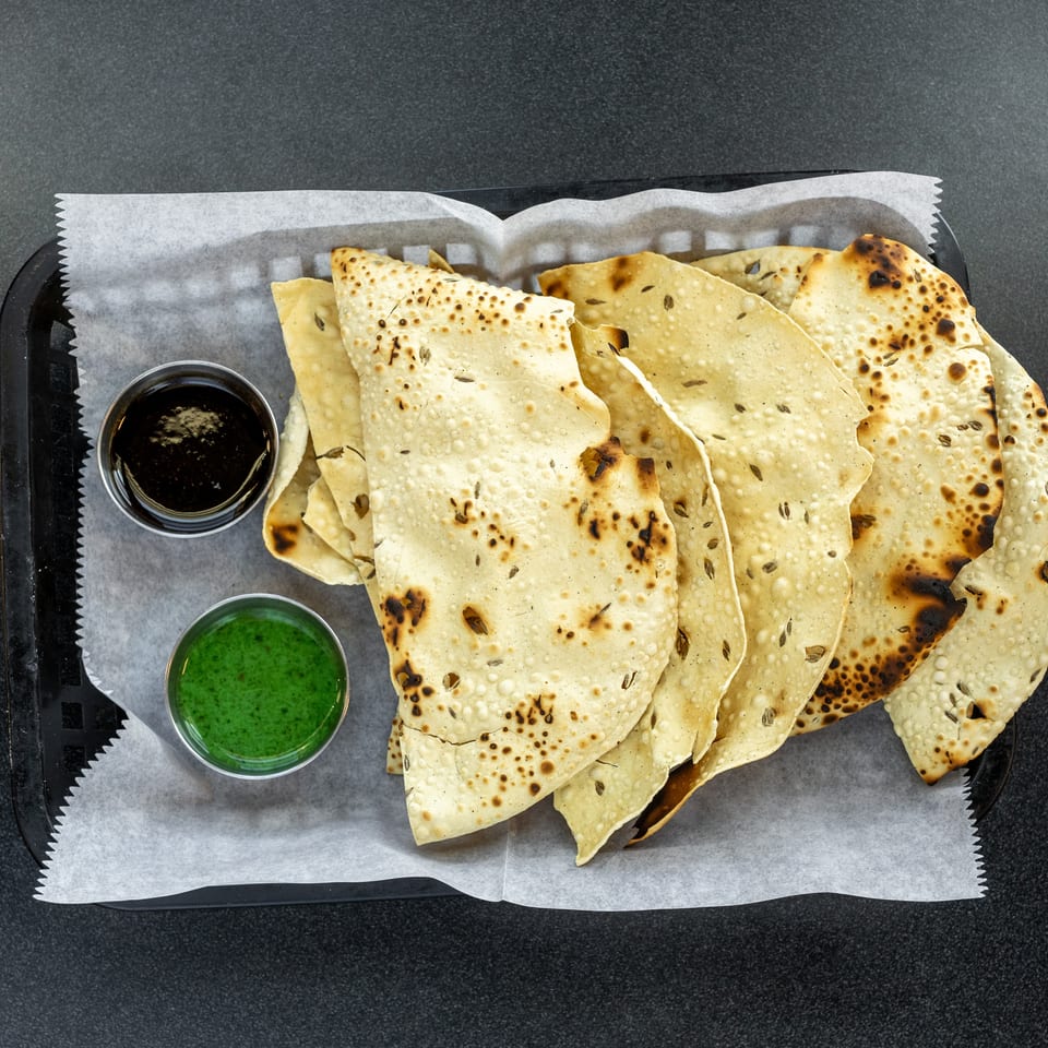 Crispy, blistered flatbreads served on parchment with dark and bright green dipping sauces.
