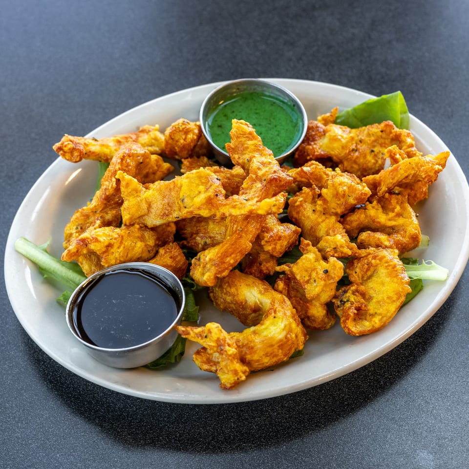Plate of golden fried appetizers with green chutney, dark dipping sauce, and lettuce garnish.